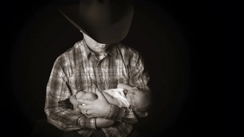 A man in a cowboy hat cradles a baby.