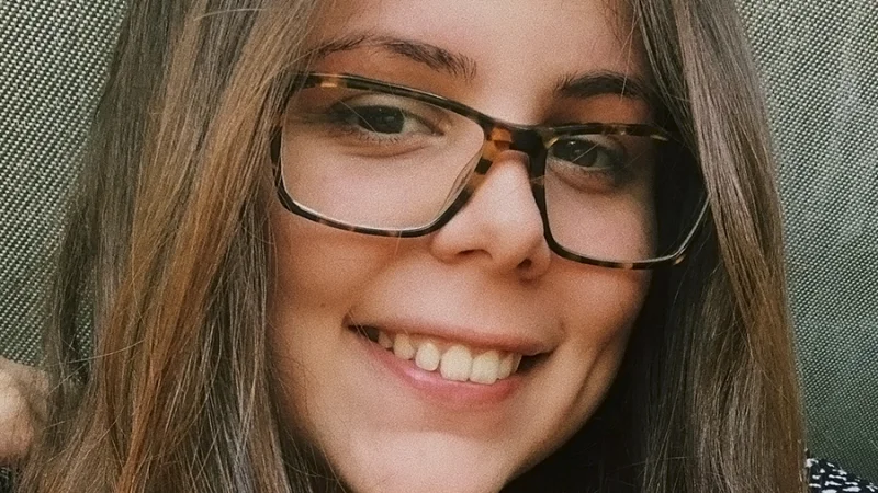 A white woman with brown hair smiles at the camera